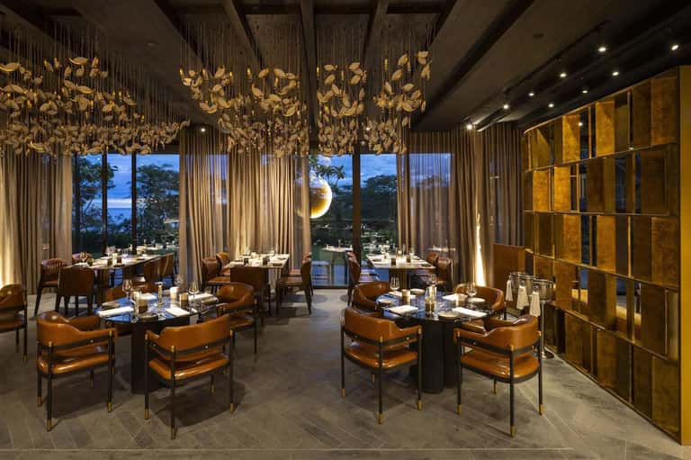 Elegant fine dining restaurant with gold sculptural ceiling, open ocean views, and upscale seating