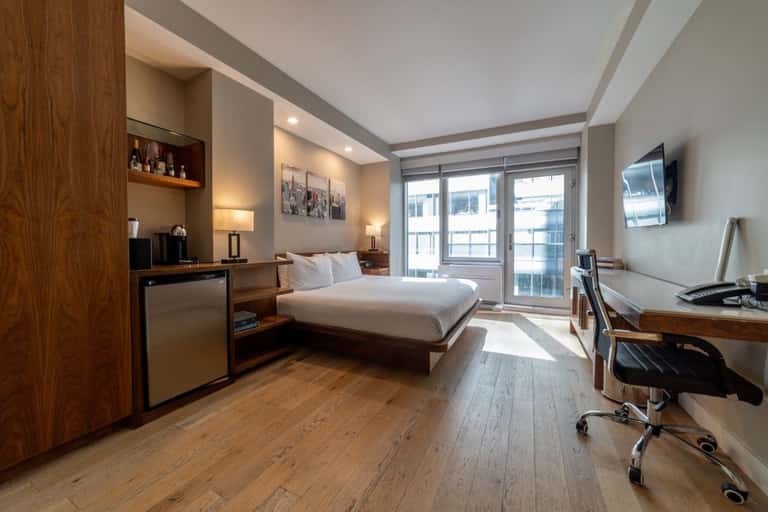 Contemporary hotel room with queen bed, wood accents, desk area, and balcony with forest views
