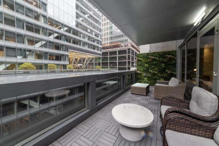 Urban hotel balcony with woven lounge chairs, living wall, and cityscape views of modern buildings