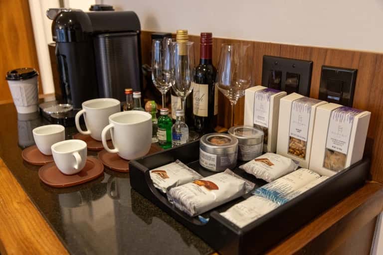 Hotel room minibar setup with coffee maker, wine glasses, snacks, and beverage amenities