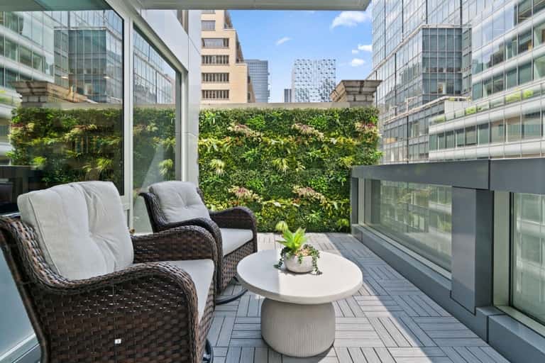 Modern balcony with woven chairs, white table, lush green living wall, and urban skyline background
