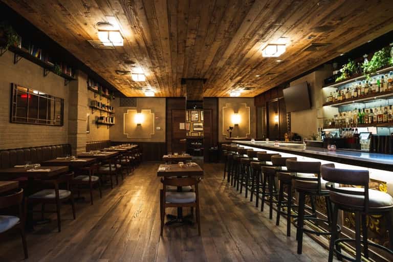 Upscale restaurant interior with wooden ceiling, dark leather booths, bar seating, and warm lighting