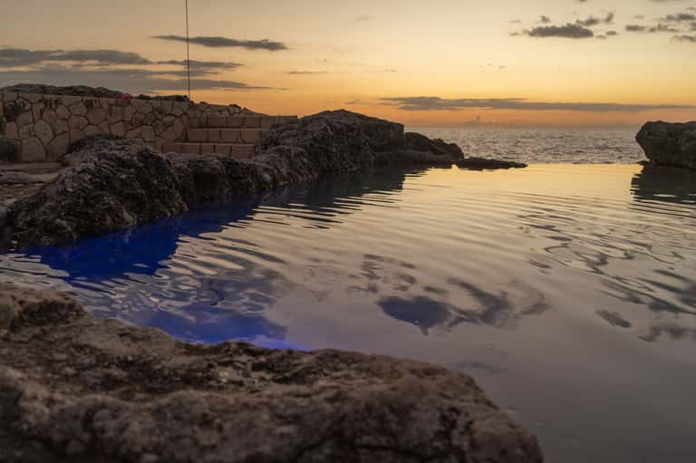 Sunset reflection on natural saltwater pool surrounded by dark rocks and coastal landscape