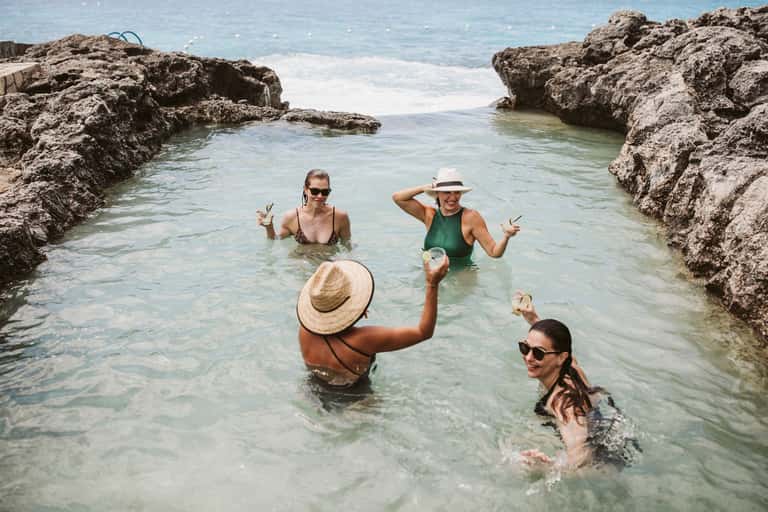 Group of guests wading and toasting in shallow turquoise water between rocky formations
