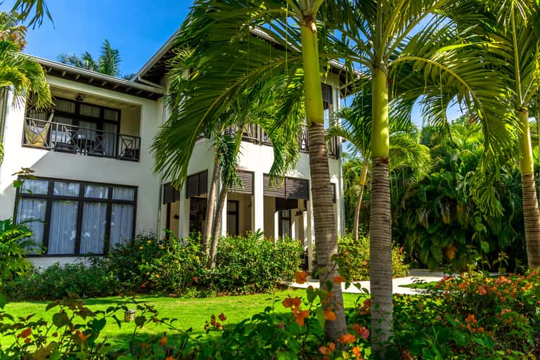 White tropical villa with tall palm trees, manicured lawn, and colorful flower gardens