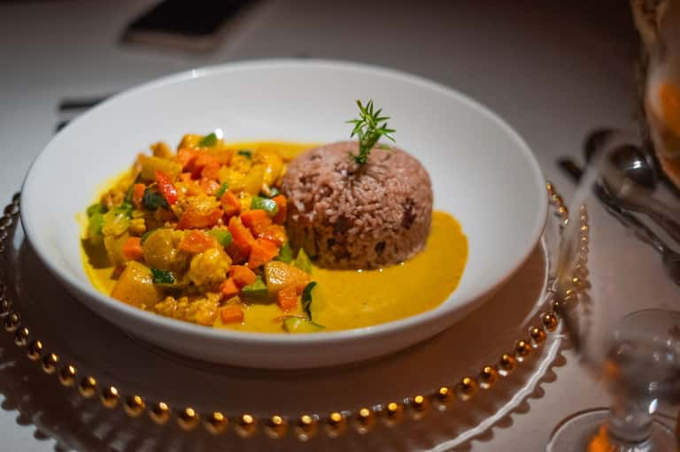 Fine dining plate with herb-crusted protein, vegetable medley in yellow sauce, and decorative plating on white dish