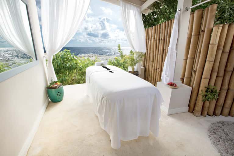 Oceanview spa treatment room with massage table, white curtains, bamboo accents, and coastal vista