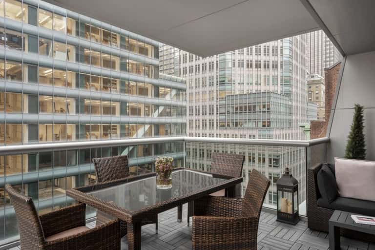 High-rise balcony with woven lounge chairs, glass table, and cityscape views of downtown office buildings