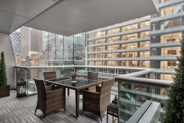 Rooftop terrace with woven furniture, glass railings, and panoramic urban skyline views during daytime