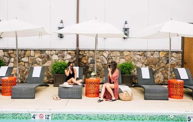 Poolside lounge seating with stone accent wall, white umbrellas, gray loungers, and orange decorative accents