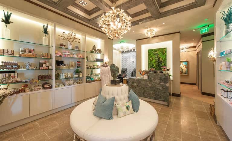 Luxury spa boutique with crystal chandeliers, retail shelves, marble reception desk, and green accent wall