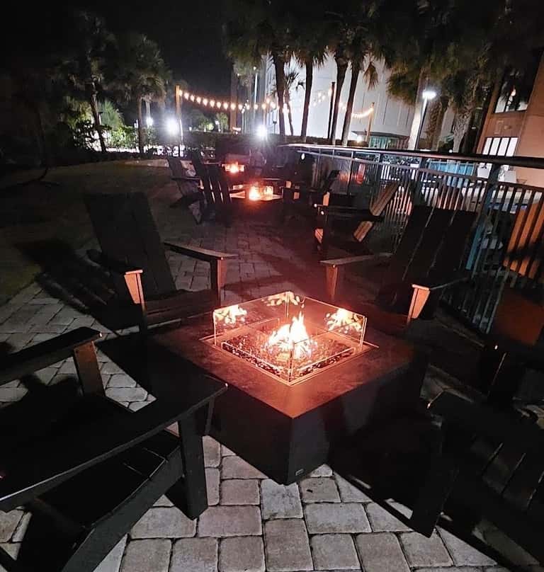 Nighttime fire pit seating area with glowing flames, Adirondack chairs, and ambient lighting in background