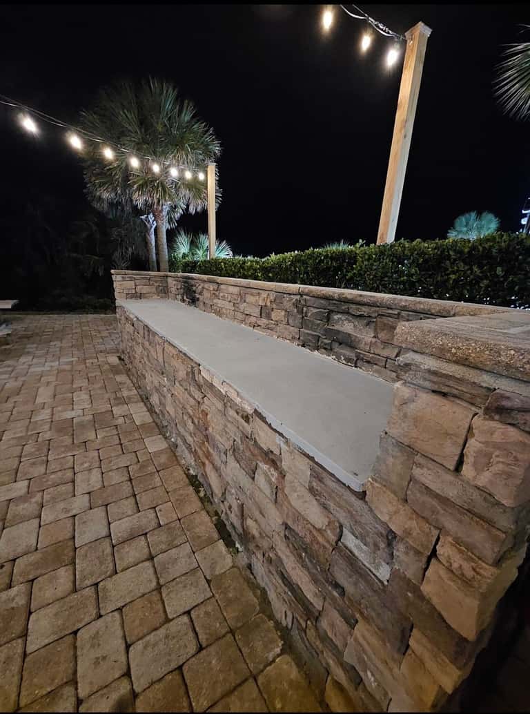 Illuminated stone retaining wall at night with string lights overhead and palm trees silhouetted