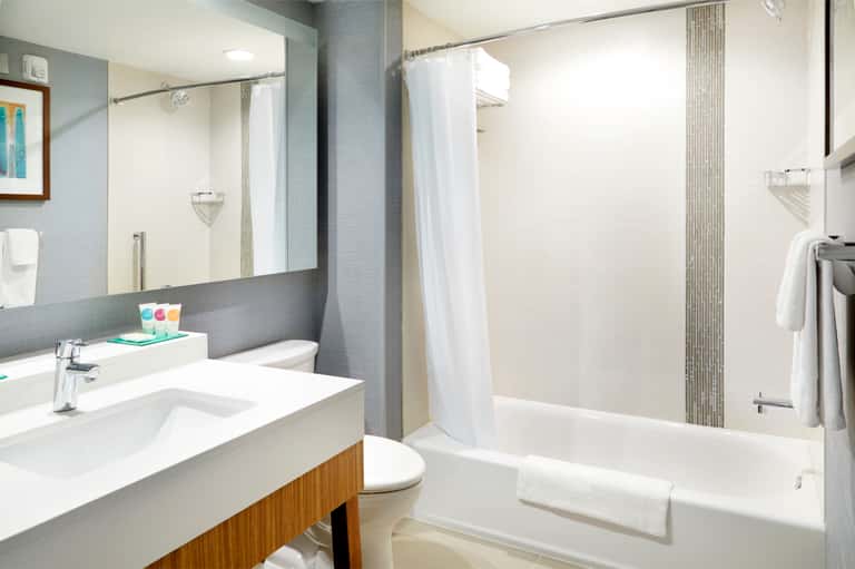 Modern bathroom with gray tile walls, white vanity, large mirror, bathtub, and shower enclosure