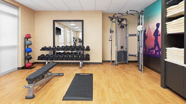 Fitness center with dumbbell racks, cable machines, treadmill, exercise bench, and motivational wall art