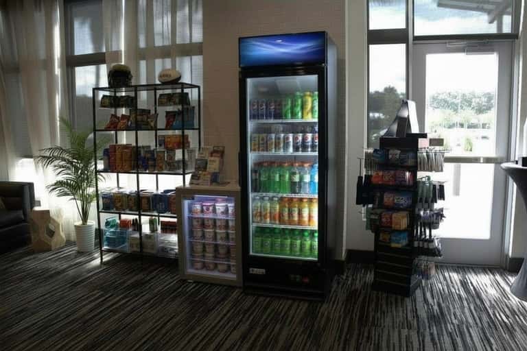 Hotel lobby area with beverage coolers, snack display, shelving with merchandise, and large windows