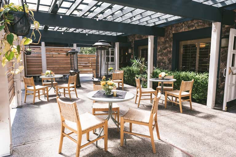 Covered patio with pergola, wooden chairs, and fire table surrounded by plants