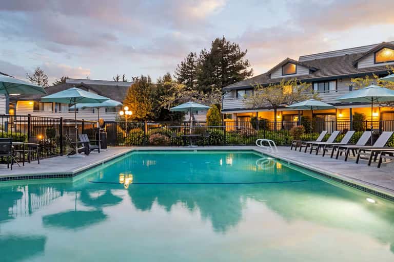 Resort pool with lounge chairs, green umbrellas, and lit buildings at twilight