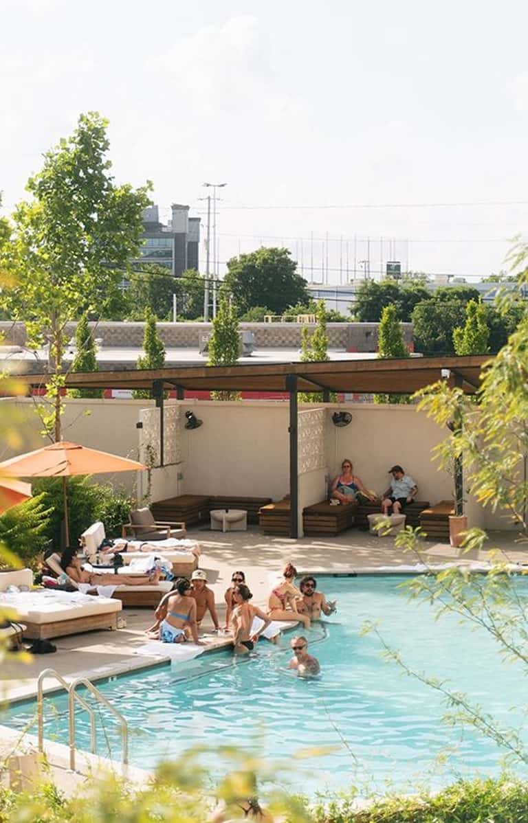 Resort rooftop pool with turquoise water, lounging areas, shade structures, and city skyline views