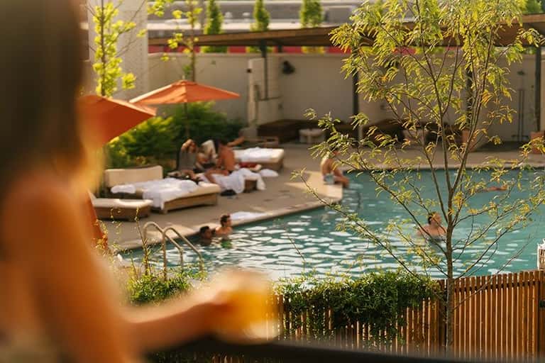 Resort pool area with swimmers, lounging guests, orange umbrellas, and covered seating areas