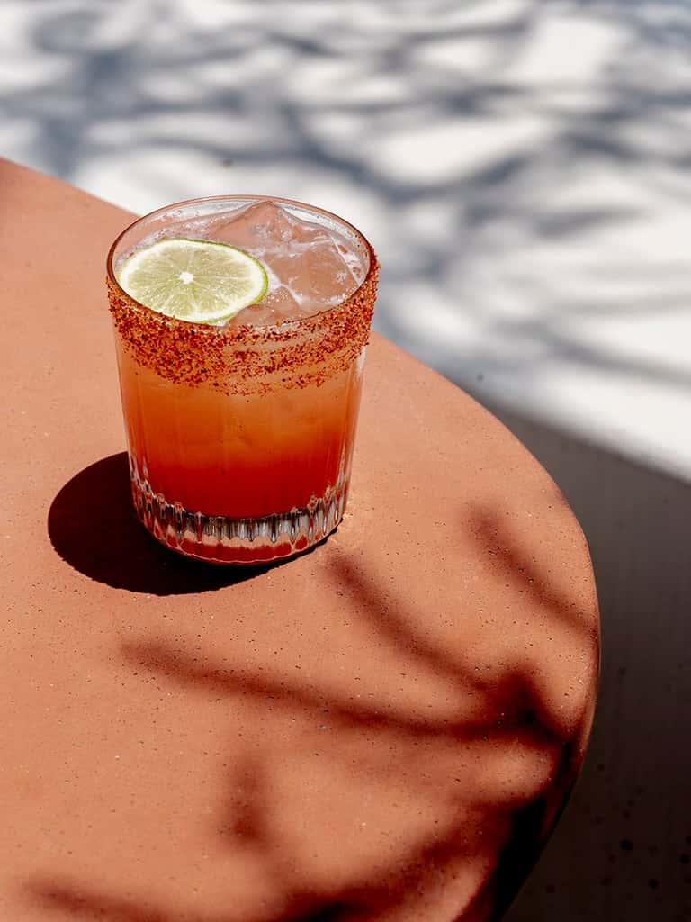 Colorful cocktail with chili-salt rim and lime slice on resort poolside decking