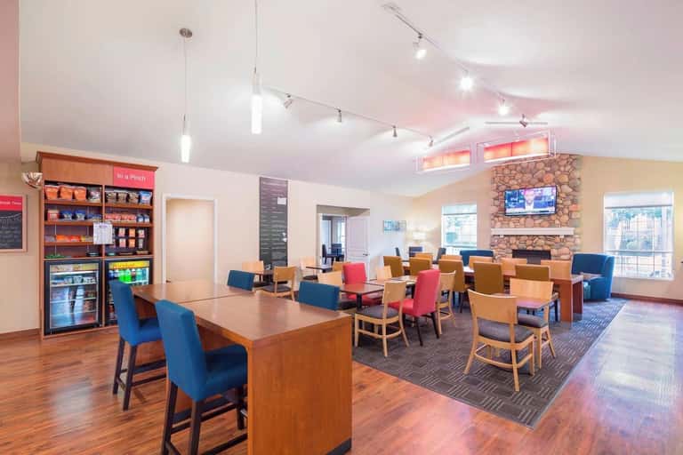 Modern hotel common area with colorful chairs, fireplace, snack station, and bright natural lighting