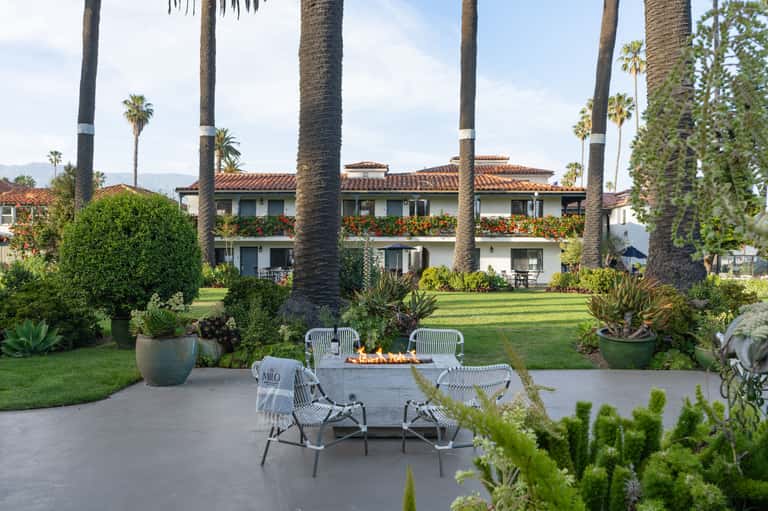 Spanish Colonial-style buildings with white stucco walls, terracotta roofs, palm trees, and fire pit seating area