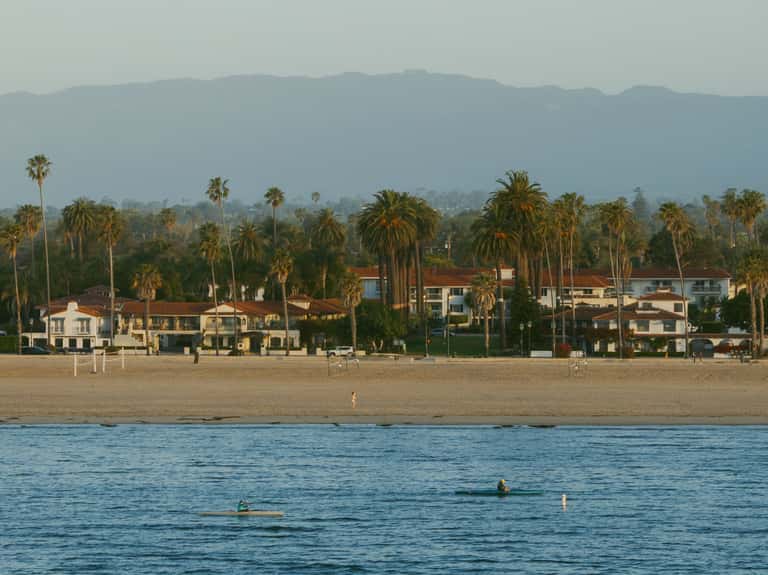 Beachfront row of Spanish Colonial homes with palm trees, mountains in background, beach and ocean in foreground
