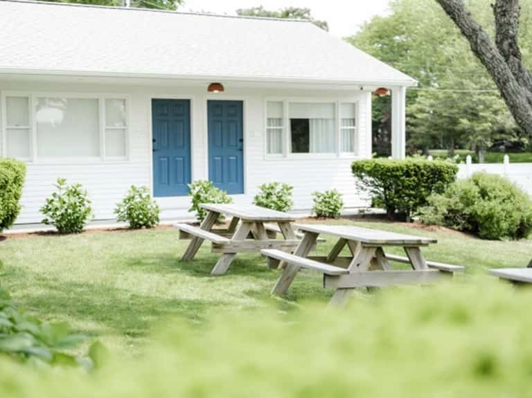 Cottage with blue doors, white exterior, picnic tables on lawn, and landscaping