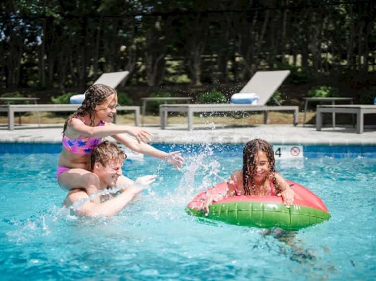 Children playing in shallow pool water with float toys and lounge chairs in background