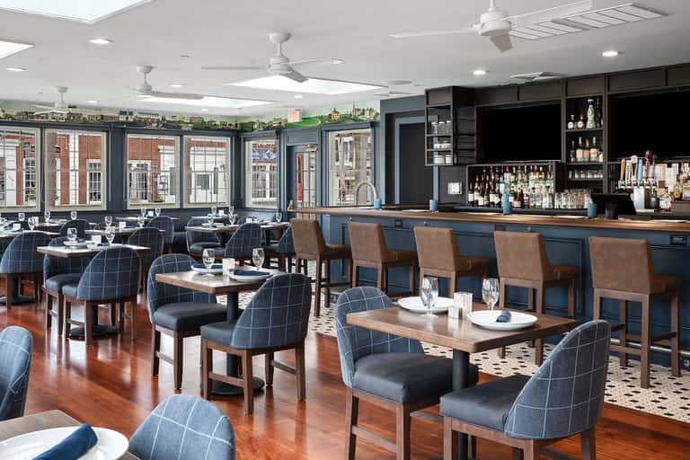 Upscale restaurant dining room with navy plaid chairs, wood tables, and full bar