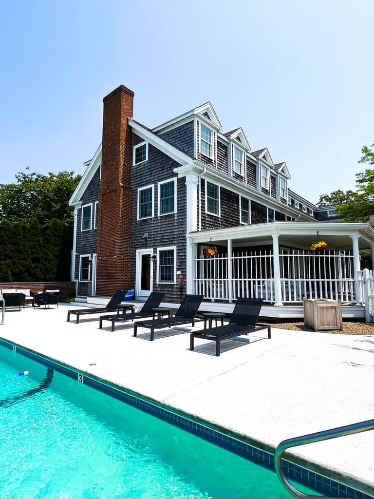 Brick house with white porch railing and multiple black lounge chairs by pool