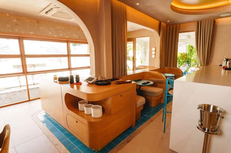 Contemporary sushi restaurant with curved wooden counter, pendant lighting, and arched doorways with ocean views
