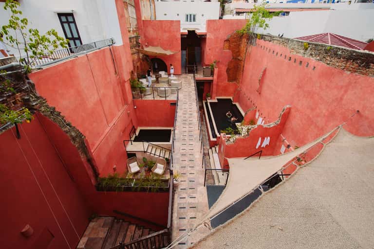 Aerial view of red-walled courtyard with terraced levels, stairs, and seating areas surrounded by white buildings