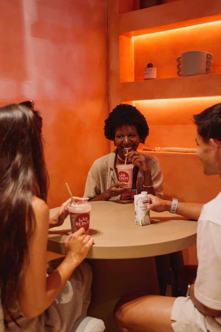 Three guests enjoying beverages at round table in glowing orange room with illuminated shelving and bright ambiance