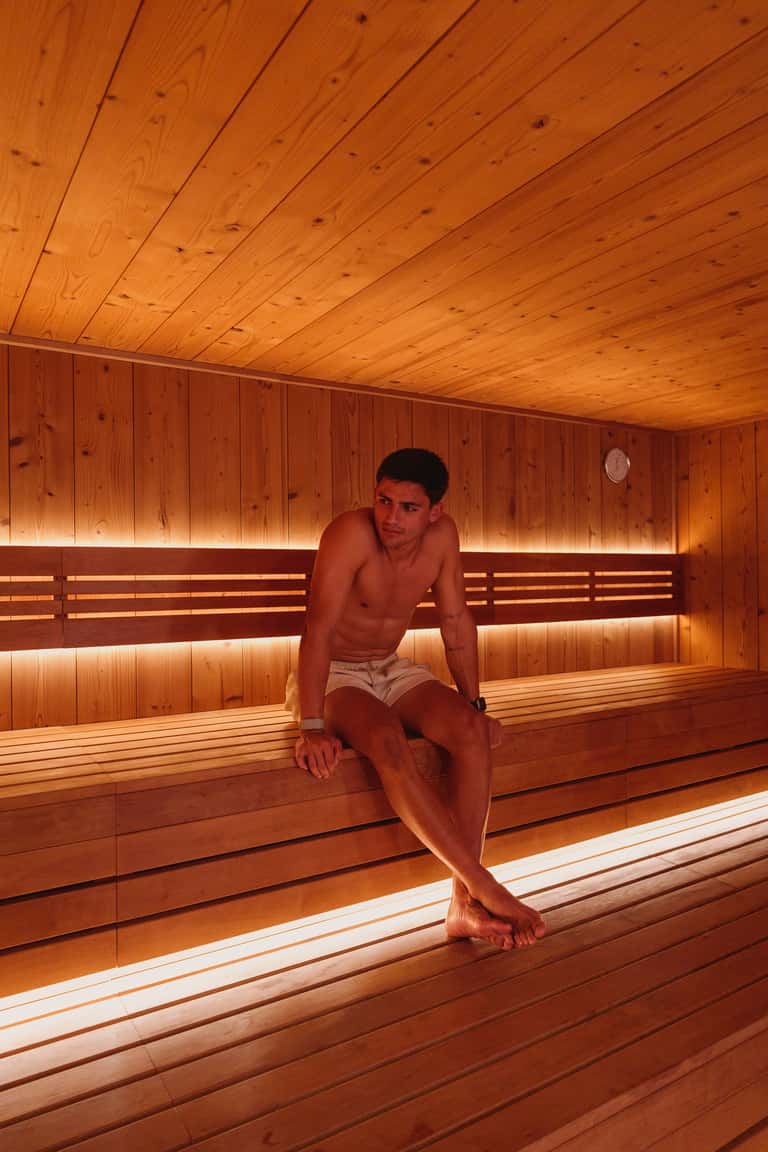 Person sitting in wooden sauna with warm lighting and wooden benches
