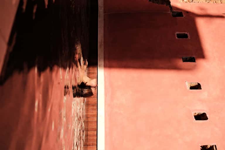 Person swimming in shallow water channel with red walls on either side