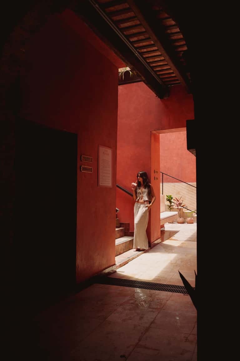 Woman in light clothing standing in doorway of red building with natural light
