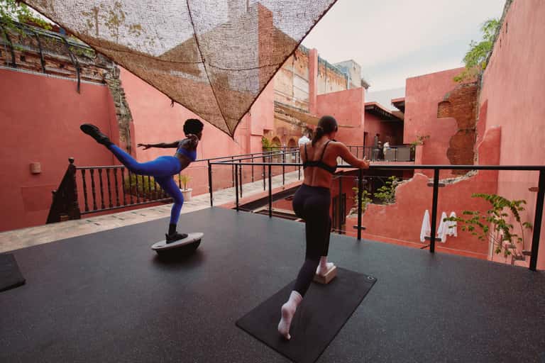 Outdoor fitness class with two women exercising on red terrace with mesh shade and red architecture