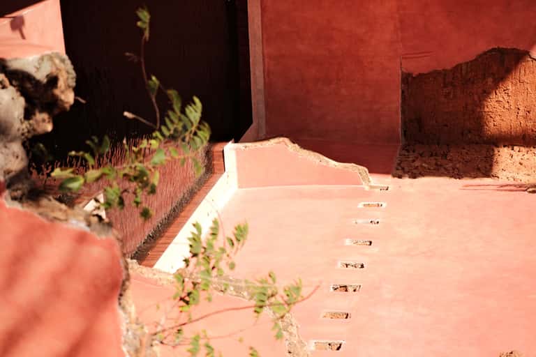 Close-up of red stucco walls, white trim, stepping stones, and wild vegetation in courtyard