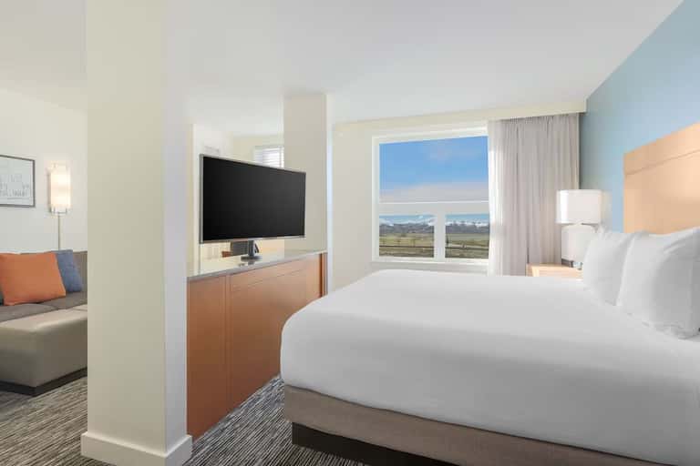Spacious hotel room with king bed, TV, sofa, and scenic mountain valley view
