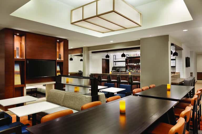 Contemporary lounge area with dark wood entertainment center, bar seating, multiple TVs, pendant lighting, and orange accent chairs