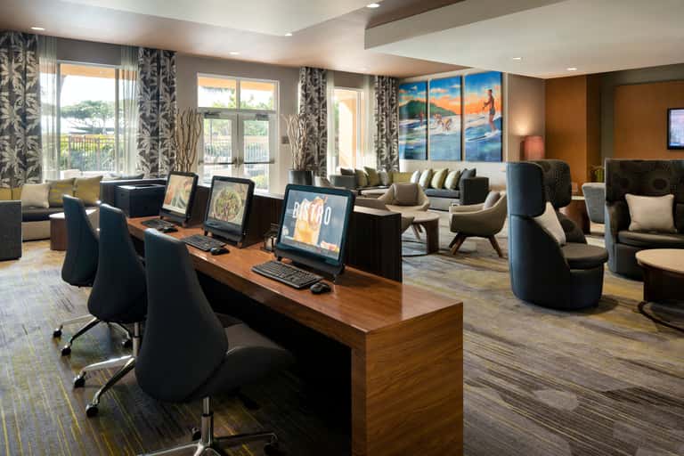 Business lounge with computer workstations, comfortable seating areas, ocean view windows with patterned curtains, and casual meeting spaces