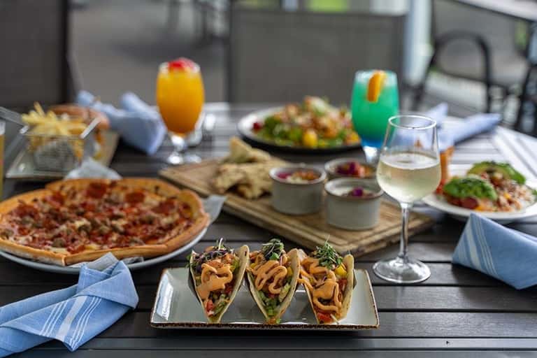 Outdoor dining table with tacos, pizza, salads, cocktails, and wine glasses on patio