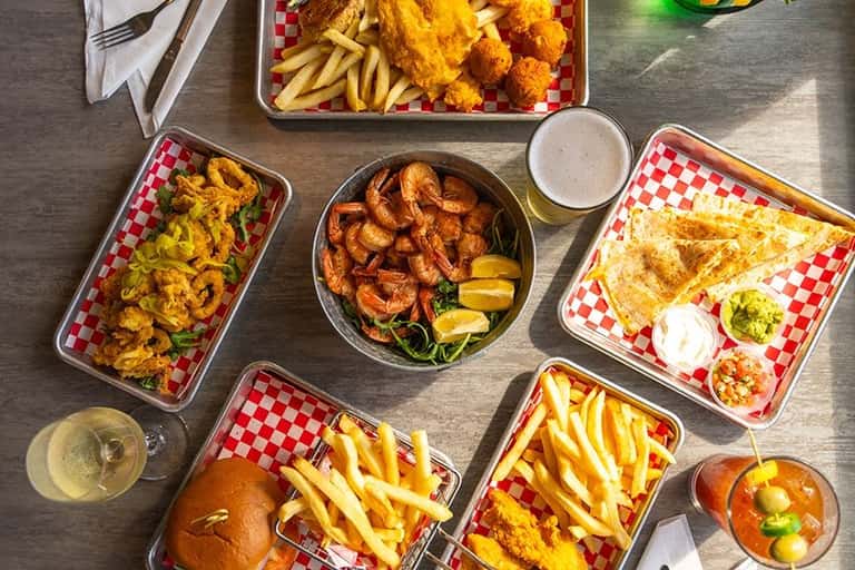 Overhead view of seafood dishes, fried chicken, fries, and beverages on red checkered paper
