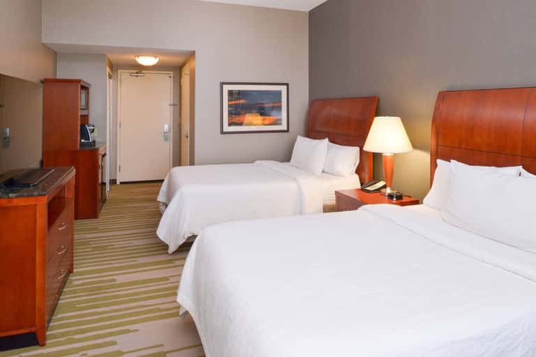 Double queen hotel room with wood furnishings, striped carpet, and entry hallway with kitchenette