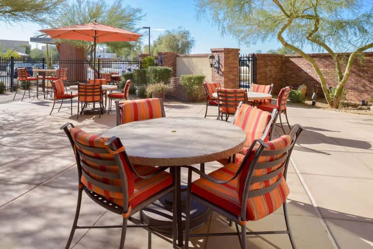 Outdoor patio with round tables, striped chairs, orange umbrellas, brick walls, and desert landscaping