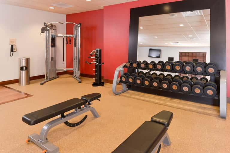 Fitness center with red accent walls, dumbbells, weight bench, and cable exercise machines