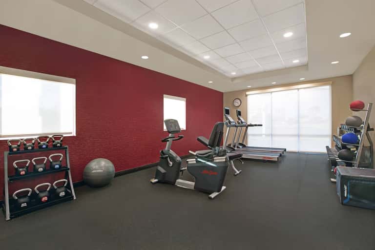 Fitness room with red walls, cardio equipment, treadmill, exercise bike, dumbbells, and stability balls