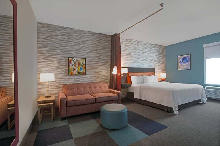 Modern hotel suite with canopy bed, orange sofa, textured wood walls, and blue accent wall